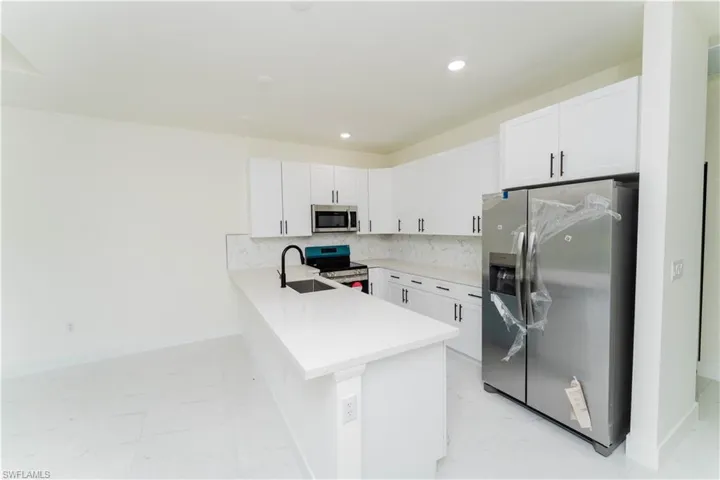 Kitchen with stainless steel appliances, a peninsula, light marble finish flooring, white cabinets, and light countertops