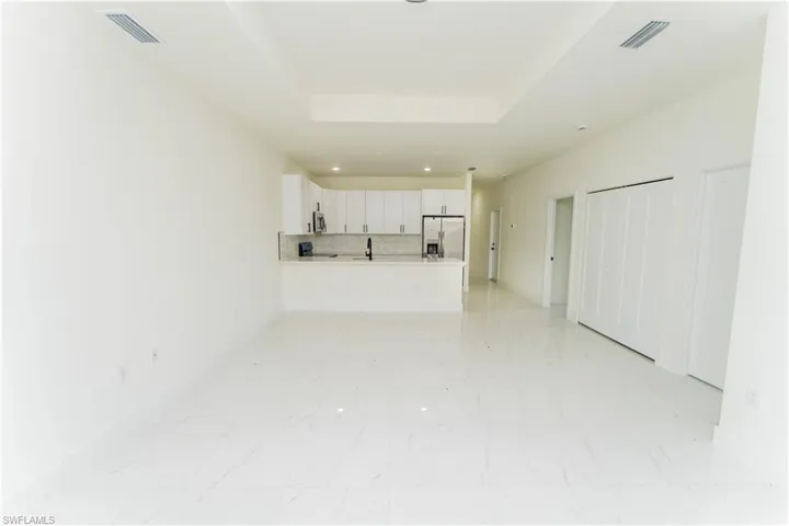 Unfurnished living room featuring recessed lighting, light marble finish floors, and a raised ceiling