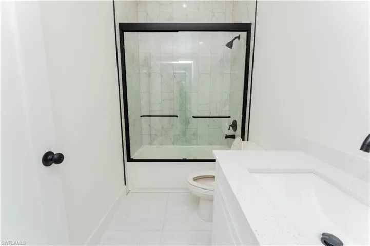 Full bath with combined bath / shower with glass door, marble look tile flooring, and vanity