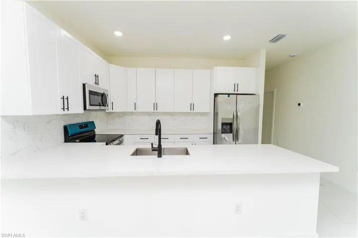 Kitchen featuring stainless steel appliances, a peninsula, white cabinets, light stone counters, and tasteful backsplash