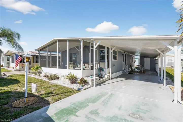Manufactured / mobile home featuring a sunroom, a carport, driveway, and a front lawn
