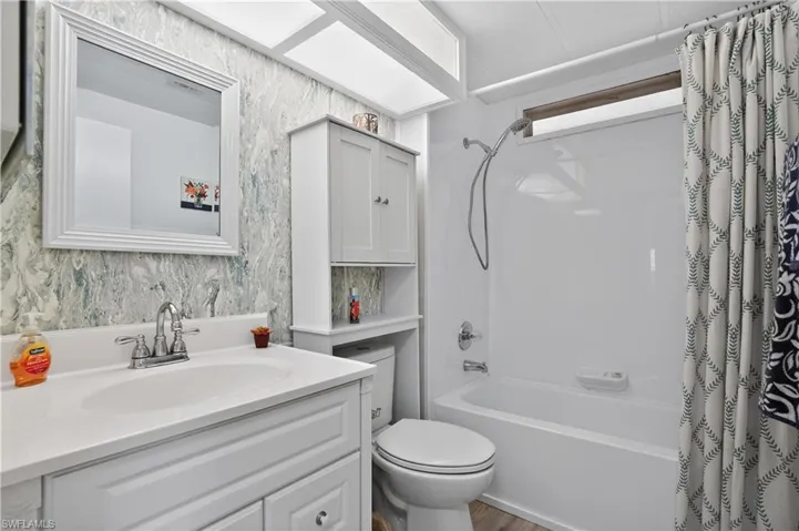 Full bath with vanity, shower / bath combo, and wallpapered walls