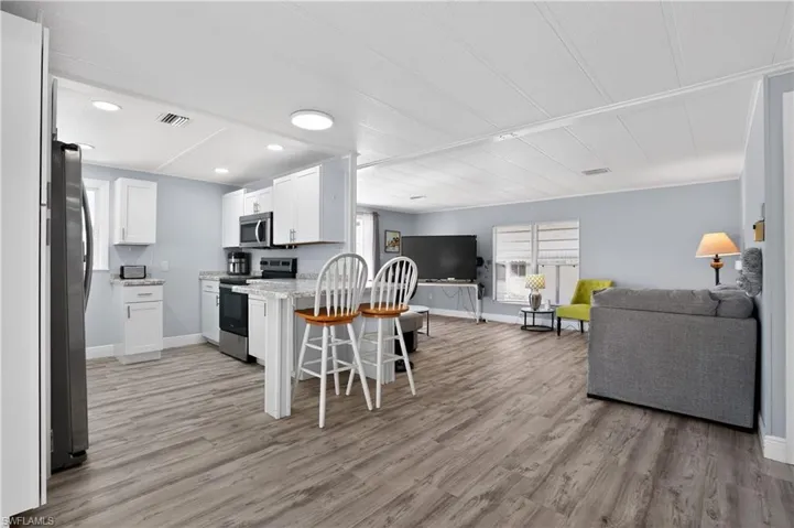 Kitchen with open floor plan, stainless steel appliances, a kitchen bar, light wood finished floors, and white cabinets