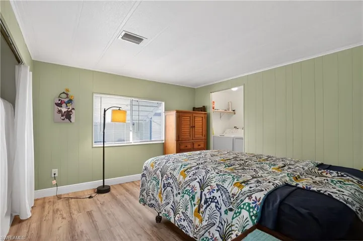 Bedroom with washing machine and dryer, wooden walls, wood finished floors, and ornamental molding