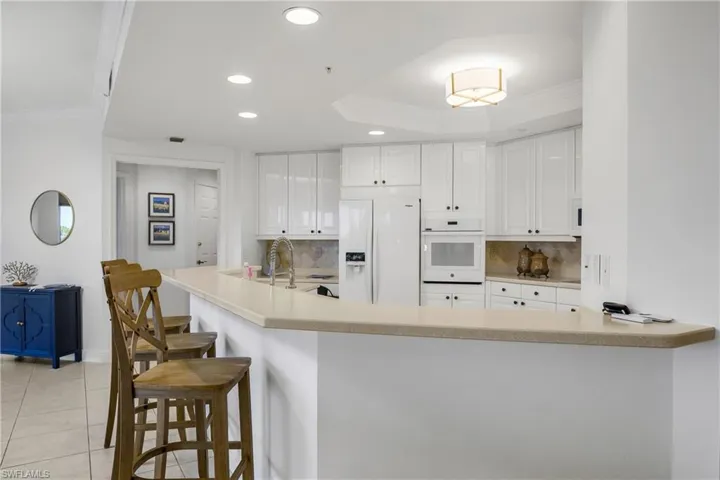 Kitchen with white cabinetry, white appliances, kitchen peninsula, and backsplash