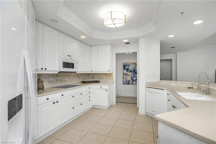 Kitchen featuring white cabinetry, sink, white appliances, and a raised ceiling