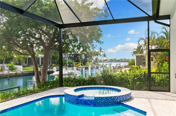 View of pool featuring a water view, a sunroom, a patio, a pool with connected hot tub, and glass enclosure