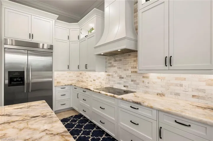 Kitchen with custom range hood, decorative backsplash, built in refrigerator, crown molding, and white cabinetry