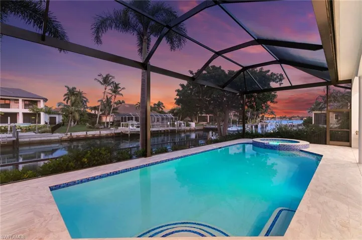 Pool at dusk with a sunroom, a water view, glass enclosure, a pool with connected hot tub, and a patio area