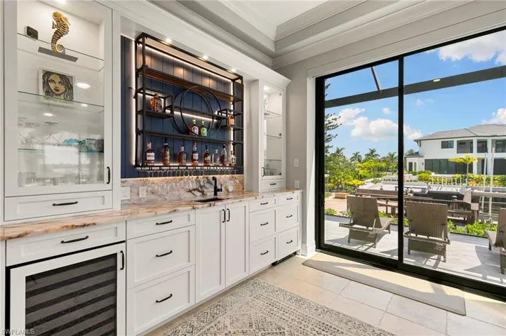 Indoor wet bar with white cabinets, beverage cooler, ornamental molding, glass insert cabinets, and light stone countertops
