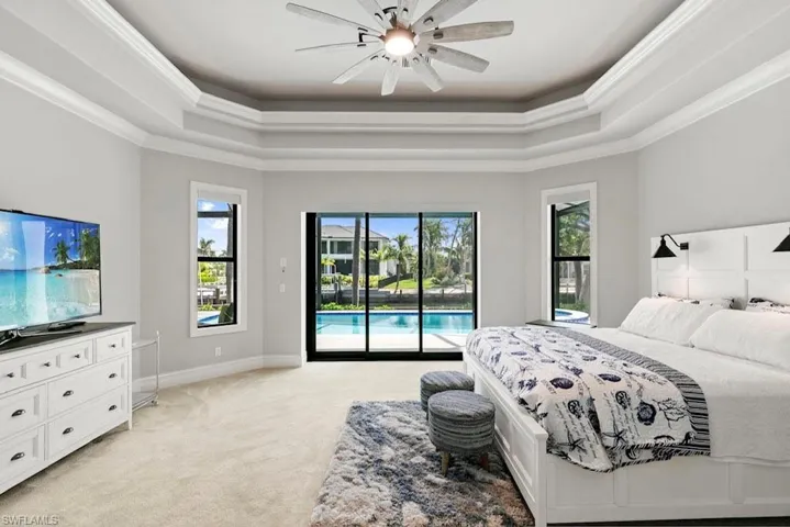 Bedroom featuring a raised ceiling, light colored carpet, multiple windows, and crown molding