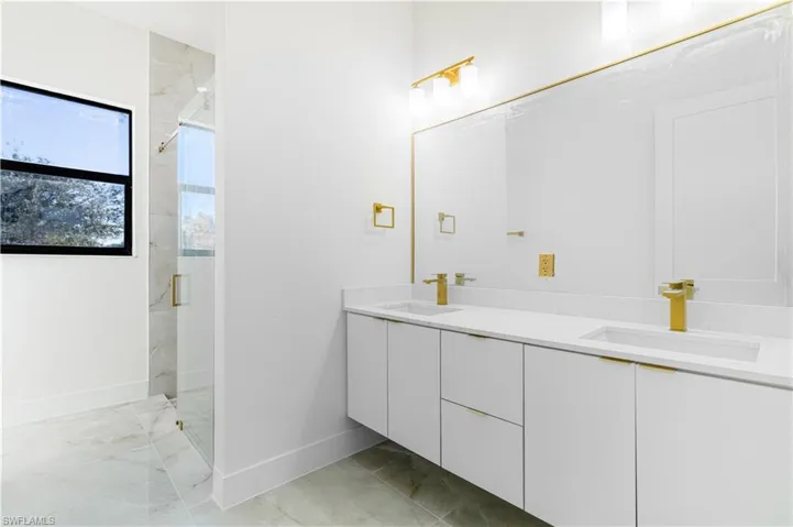 Full bath featuring double vanity, a marble finish shower, and light marble finish flooring