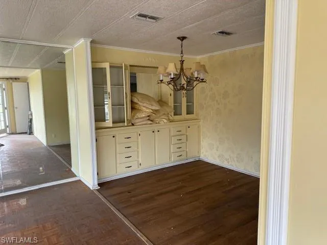 Unfurnished dining area featuring a textured ceiling, crown molding, and a notable chandelier