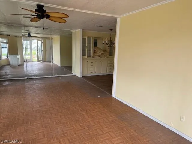 Spare room with ceiling fan with notable chandelier, parquet floors, a textured ceiling, and ornamental molding