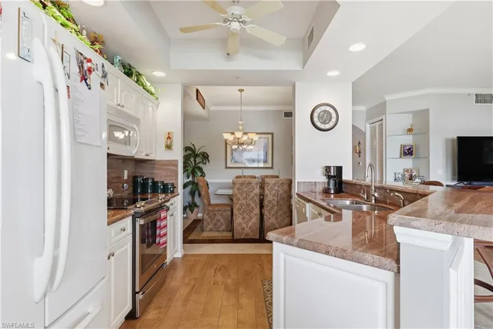 Kitchen with white appliances, white cabinetry, hanging light fixtures, a breakfast bar area, and ornamental molding
