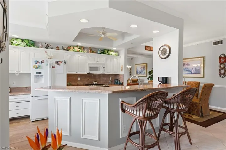 Kitchen featuring crown molding, decorative backsplash, light stone countertops, white appliances, and recessed lighting