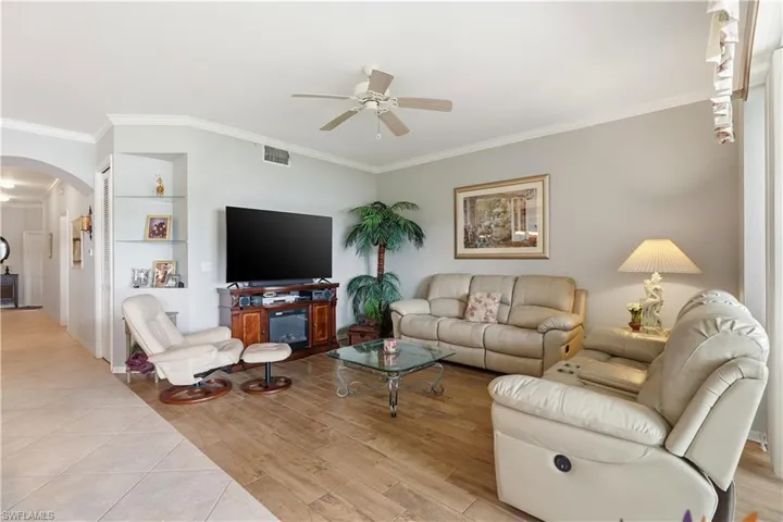 Living area with ornamental molding, arched walkways, a ceiling fan, and light tile patterned floors