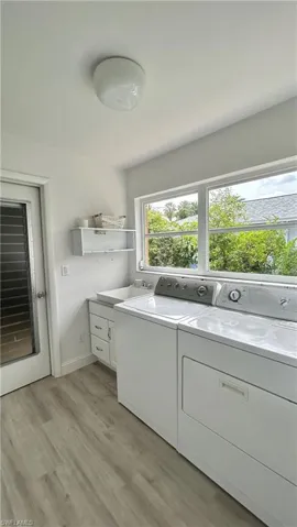 Clothes washing area featuring a healthy amount of space, sunlight, hardwood / wood-style floors, washer and clothes dryer, sink, and cabinets.
