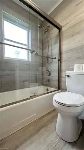 Bathroom featuring combined bath / shower with glass door, wood-type flooring, and toilet