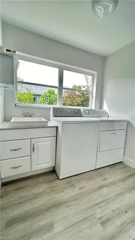 Clothes washing area with view of sink, separate washer and dryer, front of cabinets, shelf and light wood-type flooring