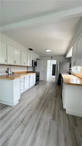 Kitchen featuring stainless steel appliances, butcher block counters, white cabinets, sink, and light hardwood / wood-style flooring