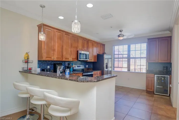 Kitchen featuring tasteful backsplash, wine cooler, kitchen peninsula, pendant lighting, and appliances with stainless steel finishes