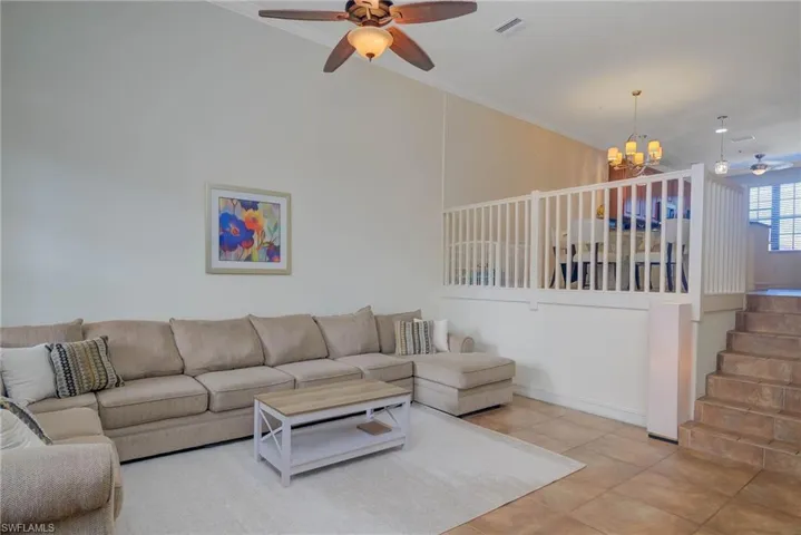 Tiled living room featuring ceiling fan with notable chandelier and ornamental molding