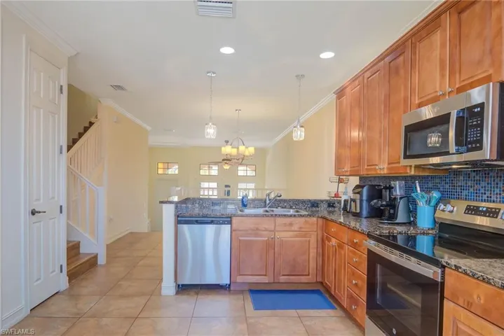 Kitchen with kitchen peninsula, ornamental molding, stainless steel appliances, sink, and decorative light fixtures