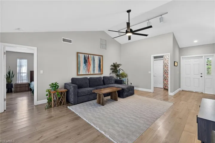 Living room featuring healthy amount of natural light, light wood-style flooring, a ceiling fan, vaulted ceiling, and rail lighting