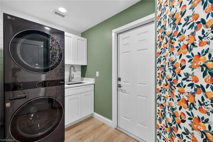 Laundry room with stacked washer / drying machine, cabinet space, and light wood-type flooring