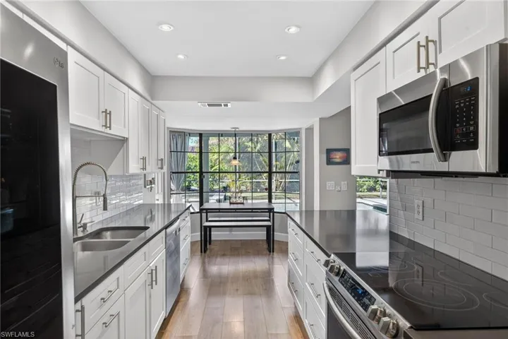 Kitchen featuring stainless steel appliances, backsplash, dark stone counters, white cabinets, and light wood-type flooring
