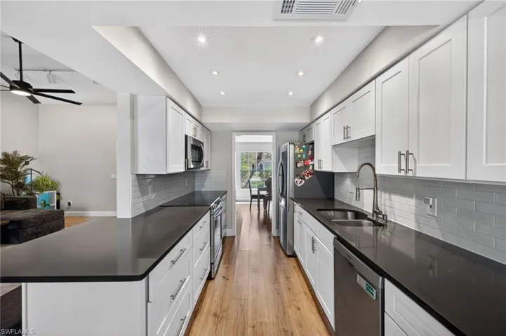 Kitchen with stainless steel appliances, light wood-style floors, recessed lighting, dark stone countertops, and white cabinets