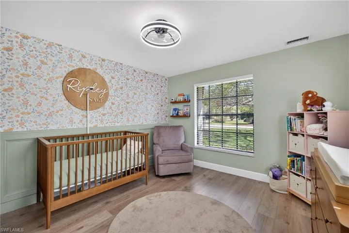 Bedroom with wallpapered walls, wood finished floors, a crib, wainscoting, and an accent wall