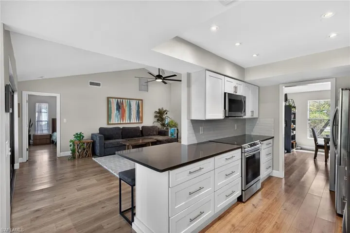 Kitchen featuring stainless steel appliances, a breakfast bar area, open floor plan, backsplash, and white cabinetry