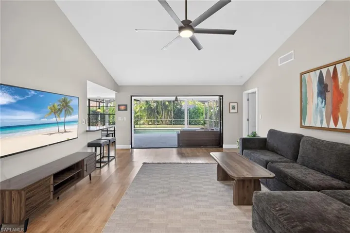 Living area with a sunroom, a ceiling fan, light wood finished floors, and vaulted ceiling