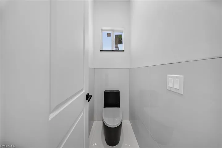 Wall-mounted toilet with a contrasting black tank and white bowl, complemented by high-gloss white wall tiling and a white paneled door with a black handle
