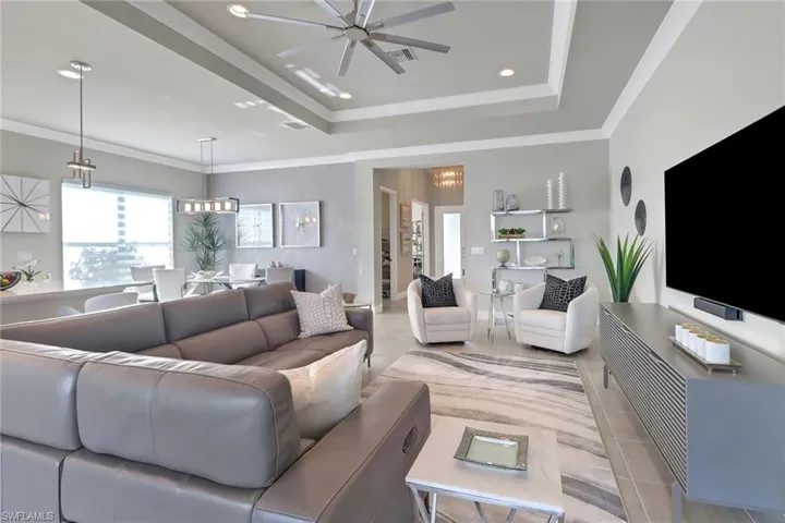 Tiled living room with ceiling fan with notable chandelier, crown molding, and a tray ceiling
