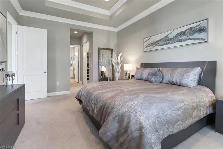 Bedroom featuring crown molding, ensuite bathroom, light colored carpet, and a closet