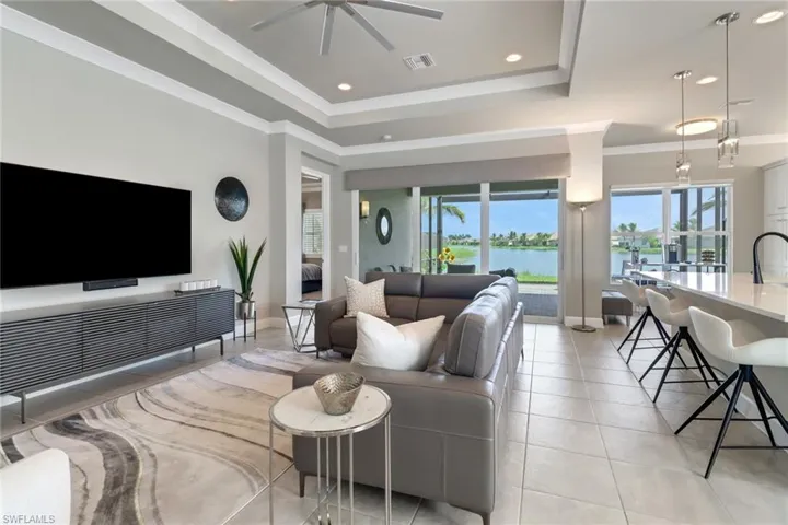 Tiled living room featuring a raised ceiling, ceiling fan, ornamental molding, and a water view