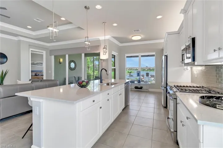 Kitchen with a center island with sink, pendant lighting, stainless steel appliances, sink, and white cabinetry