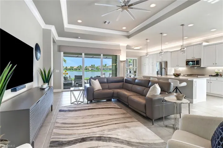 Living room featuring ceiling fan, a raised ceiling, light tile patterned flooring, and ornamental molding