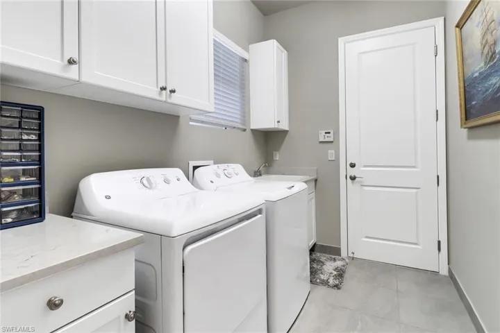 Laundry room with cabinets, sink, light tile patterned floors, and washing machine and dryer