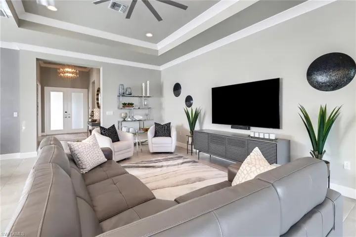 Tiled living room with ceiling fan with notable chandelier and a raised ceiling