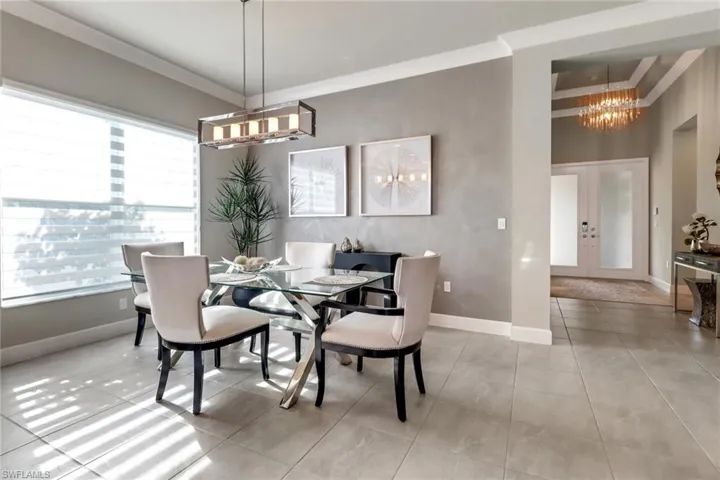 Tiled dining space with ornamental molding, french doors, and a chandelier