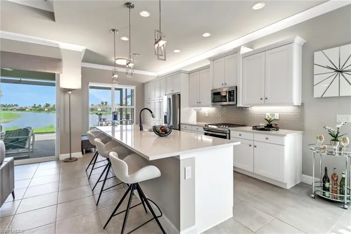 Kitchen featuring white cabinets, appliances with stainless steel finishes, a water view, pendant lighting, and a kitchen island with sink