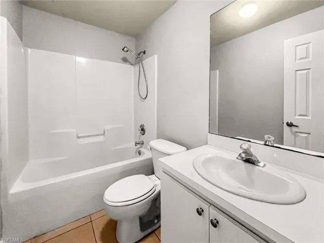 Bathroom featuring a white vanity with an integrated sink, a large wall-mounted mirror, a toilet, a full bathtub with an overhead shower, and neutral tile flooring