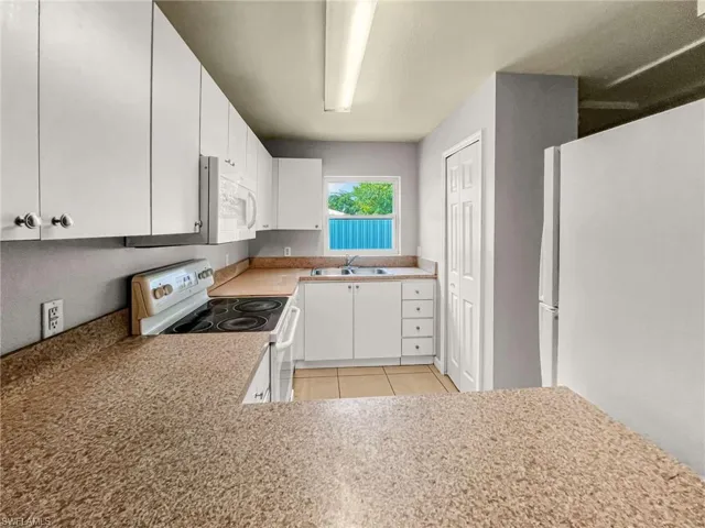 Kitchen featuring white cabinetry, speckled countertops, a double basin sink, white appliances, and tile flooring