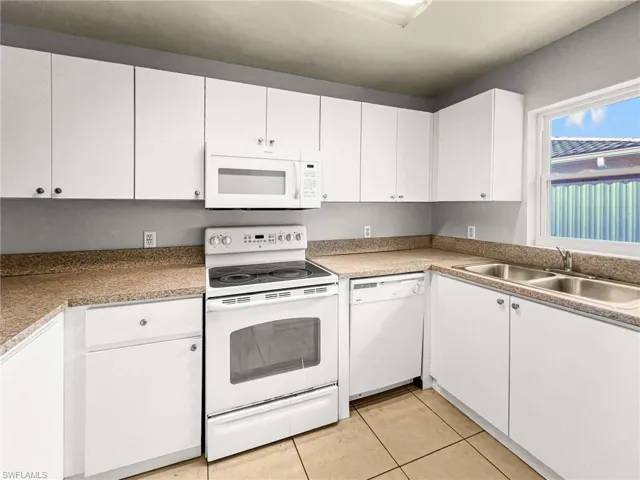 Kitchen featuring white cabinetry, solid surface countertops, tile flooring, a double basin stainless steel sink, and a built-in microwave