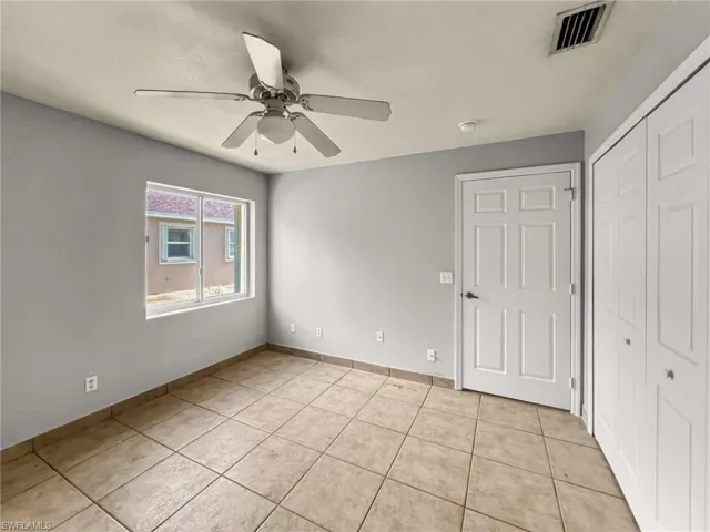 Room featuring neutral wall tones, tile flooring, a ceiling fan with integrated lighting, a window with exterior views, and bi-fold closet doors