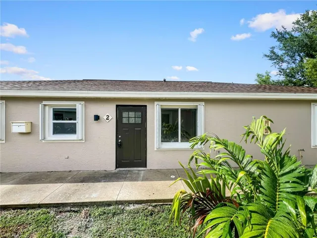 Exterior featuring a dark panel entry door with upper glass panes, light-toned stucco finish, and white-framed windows
